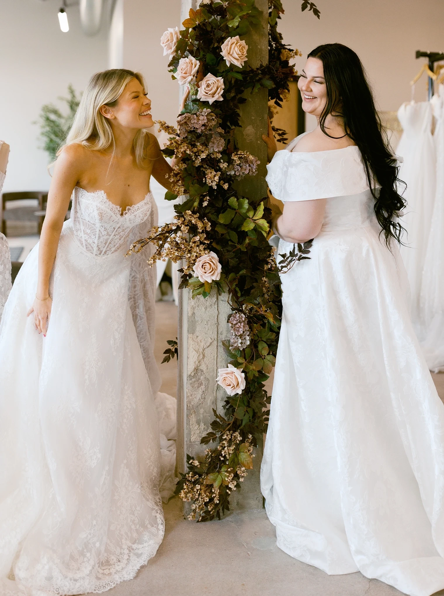 Photo of two models wearing bridal gowns posing next to a decorated wall.
